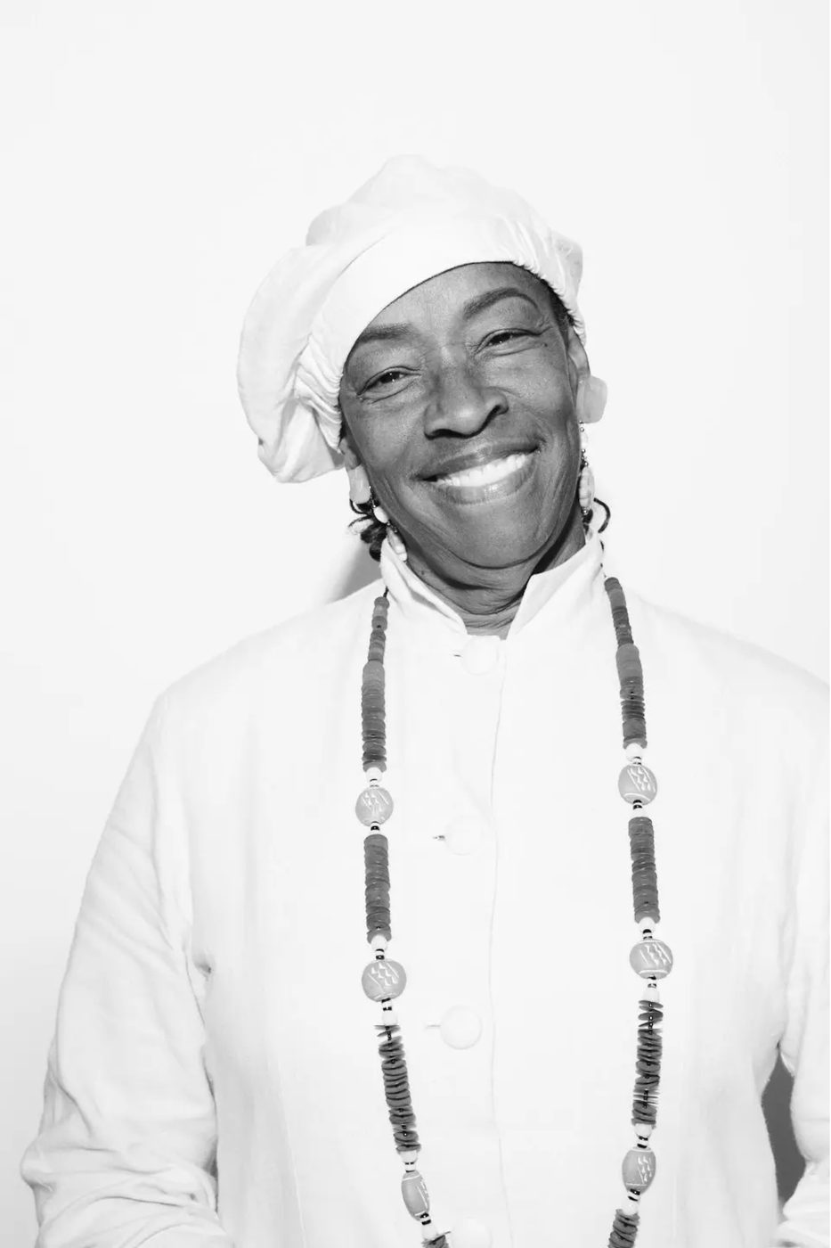 Queen Aminah in a white head wrap and long beaded necklace